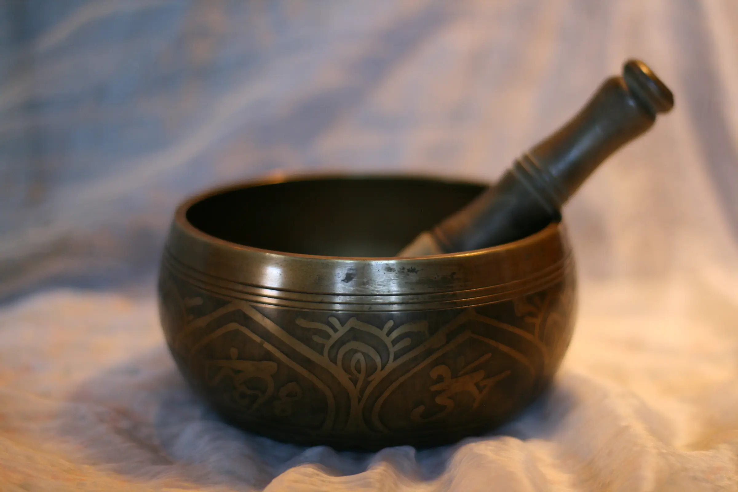 A hand-hammered singing bowl and mallet resting on soft cloth in warm light